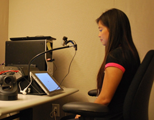 Mulher sentada em frente a um PC com dispositivo de acompanhamento dos movimentos dos olhos posicionado em sua frente
