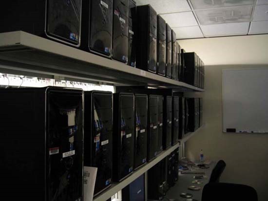A long desk and two shelves, each containing 12 or more computers